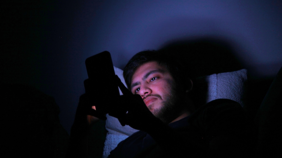 Man looking at smartphone in the dark, face lit by screen.