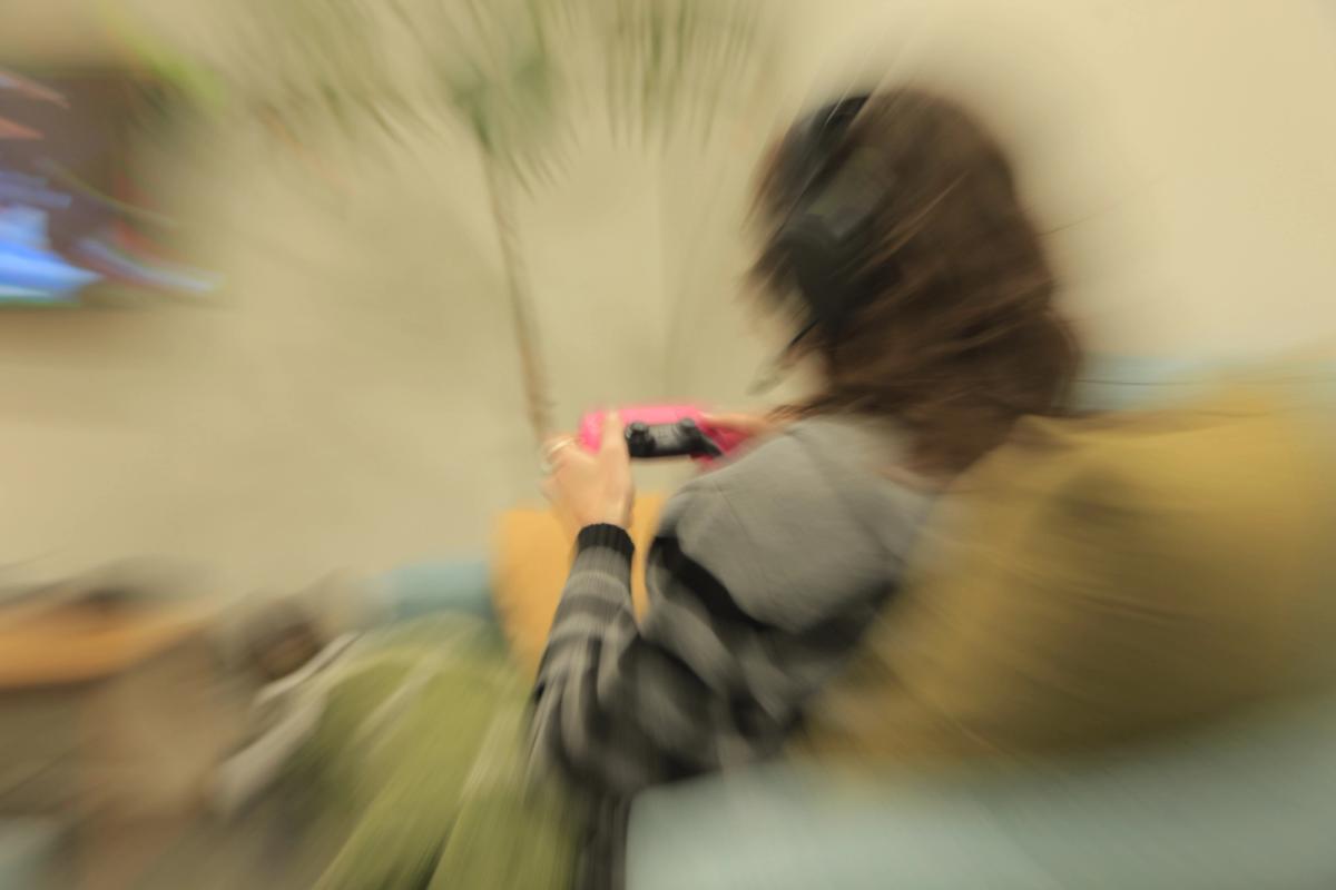 A person with headphones playing a video game on a pink handheld console, blurred with radial motion.