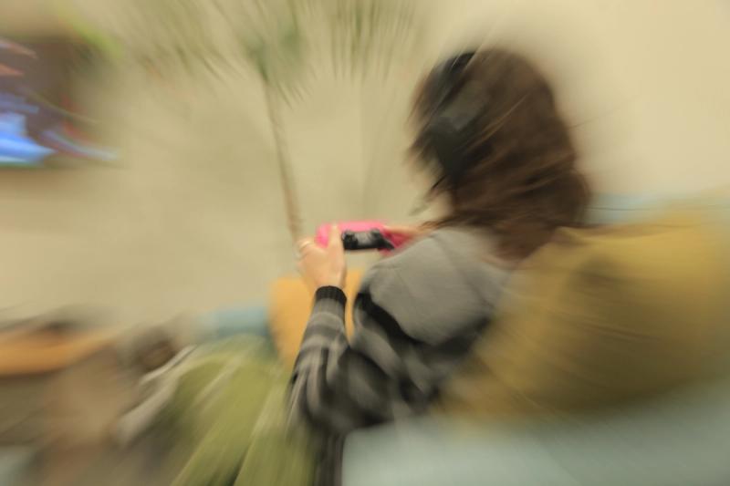 A person with headphones playing a video game on a pink handheld console, blurred with radial motion.