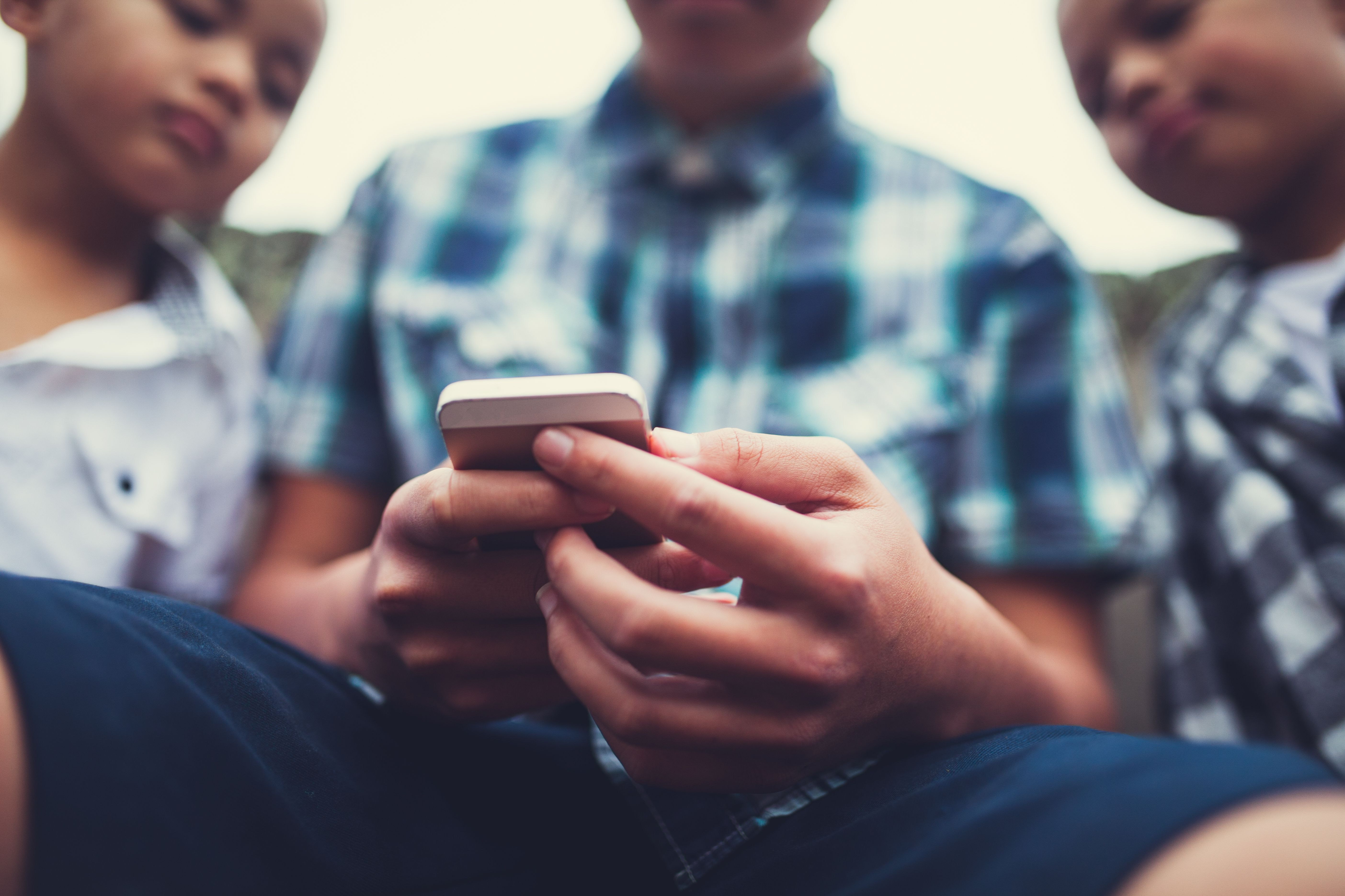Three boys gathered around a smartphone.