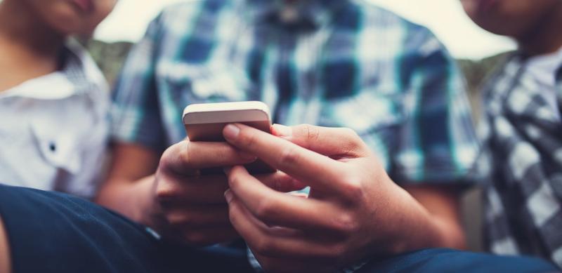 Three boys gathered around a smartphone.