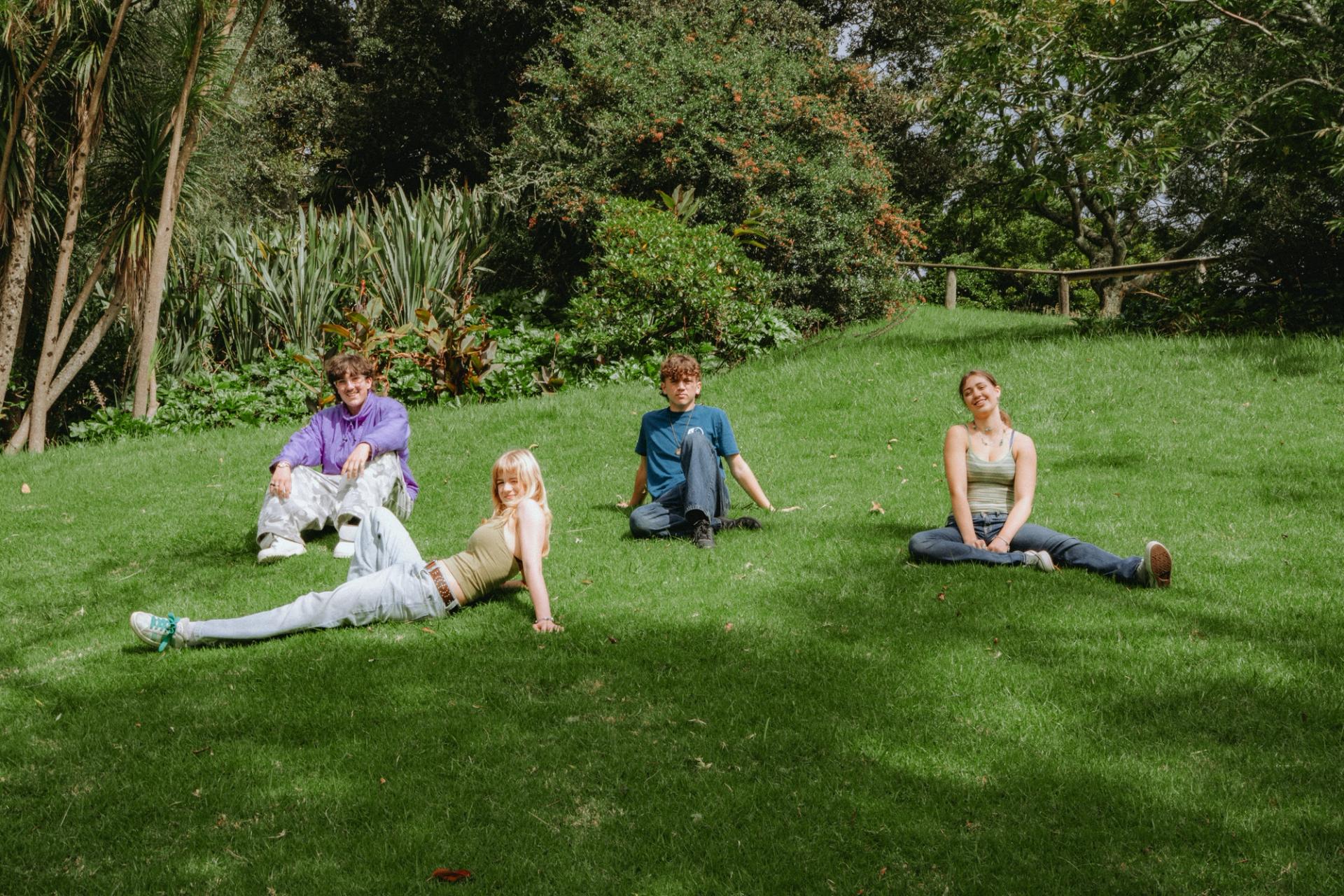 Four young people sitting and lying on a grassy hill in a park.