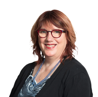 Headshot of a smiling woman with reddish-brown hair and red glasses, wearing a black cardigan and blue necklace against a white background.