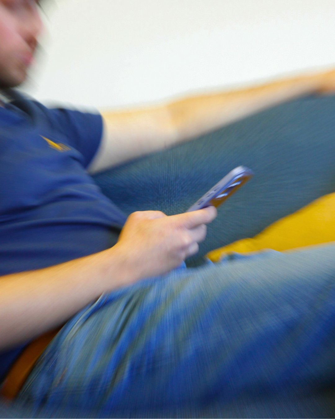 A person, heavily blurred with radial motion, is sitting in a blue shirt and jeans, holding a smartphone.