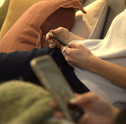 Hands of two people interacting with a smartphone and a remote control.