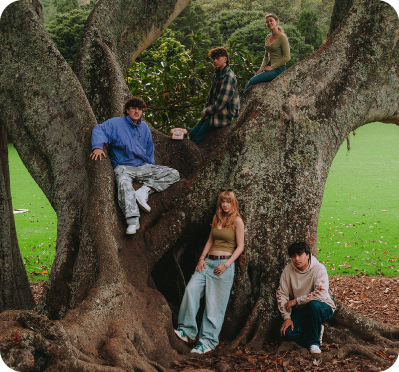 Five young people posing on and around a large mossy tree, with an antique rotary telephone on a branch.