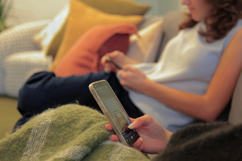 Two people sitting on a couch, each looking at a smartphone.