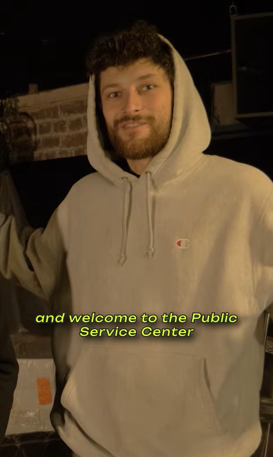A man in a gray Champion hoodie with a beard and curly hair, smiling. Text overlay: "and welcome to the Public Service Center."
