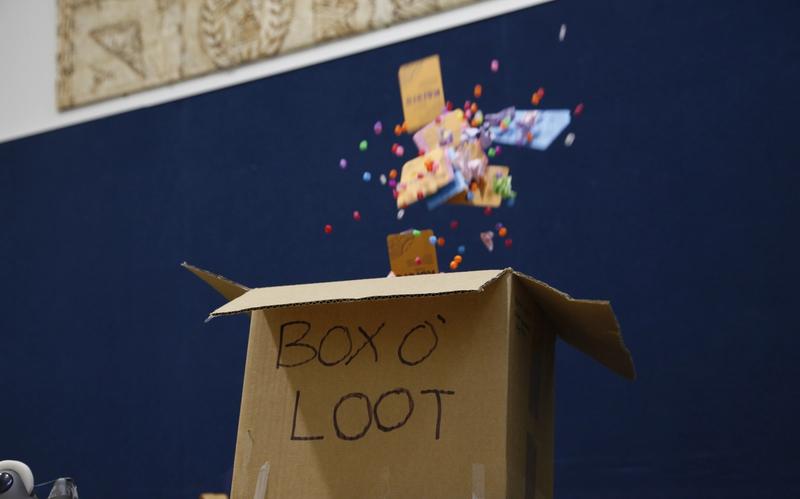 A cardboard box labeled "BOX O' LOOT" explodes with colorful pom-poms and small packages.