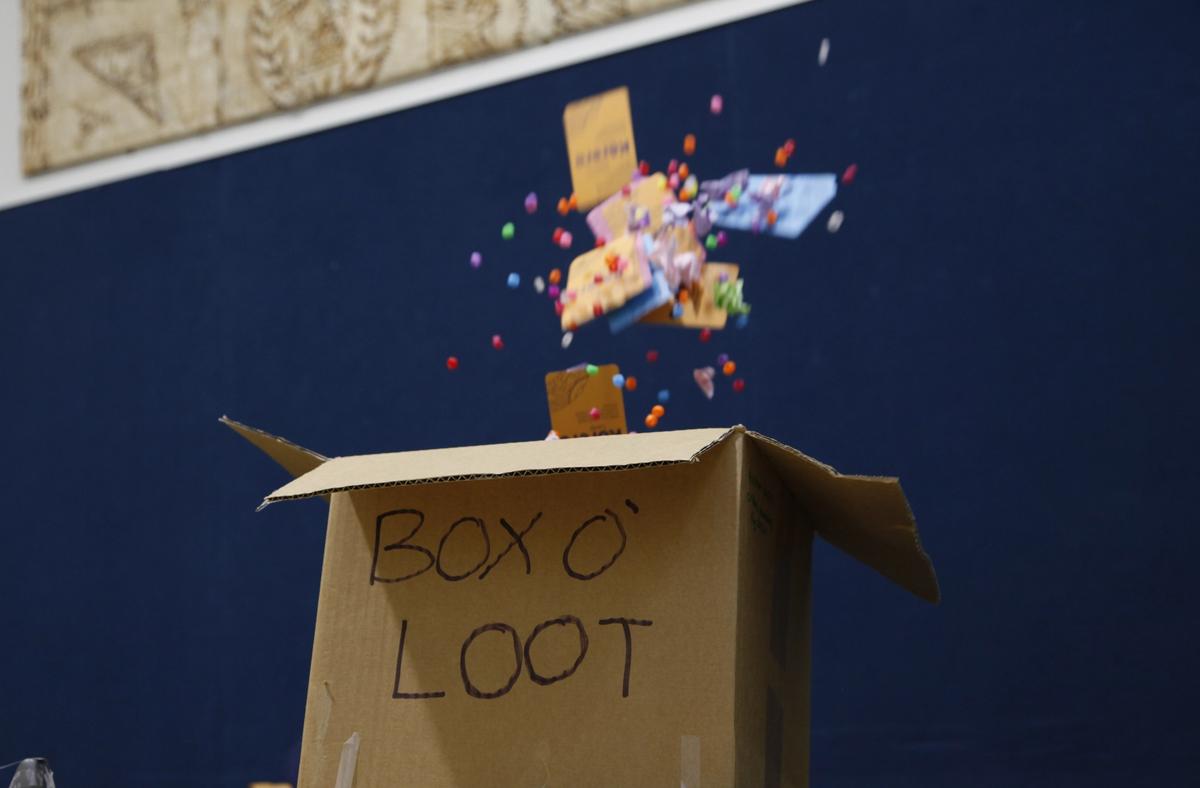 A cardboard box labeled "BOX O' LOOT" with colorful pom-poms and small items exploding upwards.