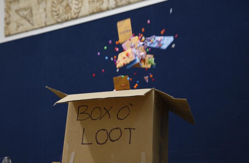 A cardboard box labeled "BOX O' LOOT" with colorful pom-poms and small items exploding upwards.