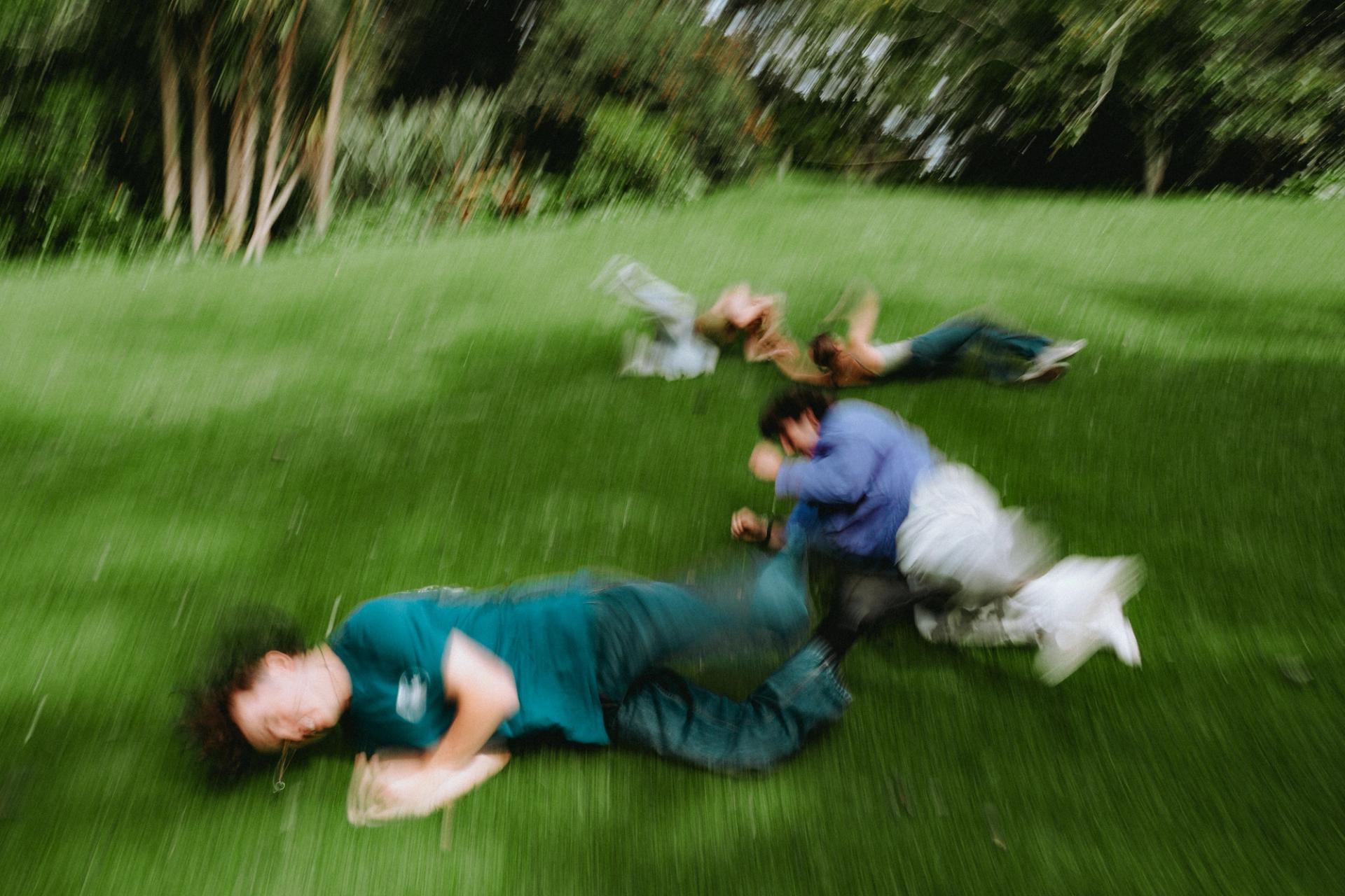 Motion-blurred image of people on green grass, appearing to run or roll.