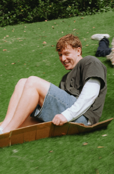 Two young men smiling as they slide and crawl down a grassy hill.
