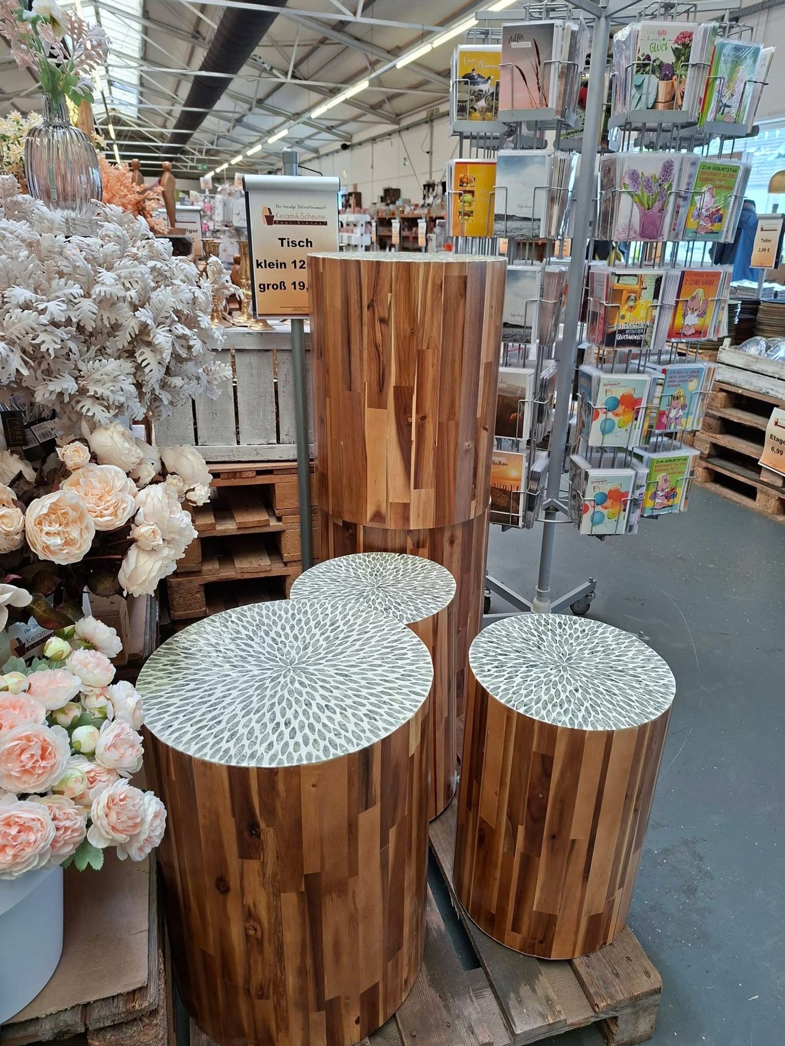 Holztische zwischen Blumen und Kartenständern in einem Geschäft.