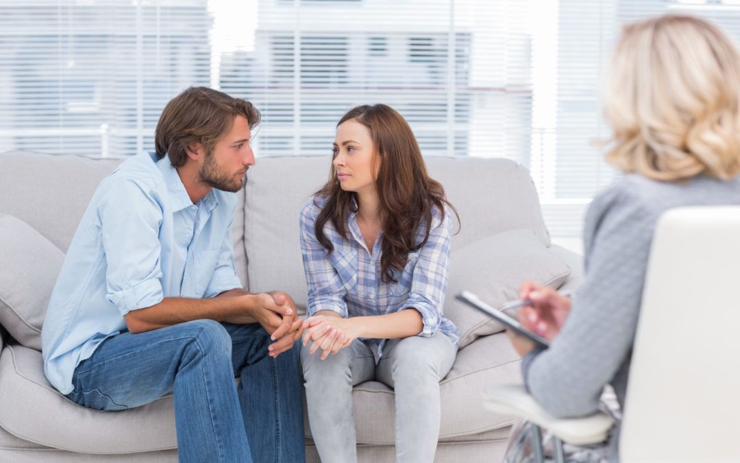 Two people seated together facing a therapist in a warm, calm office, soft daylight, unposed