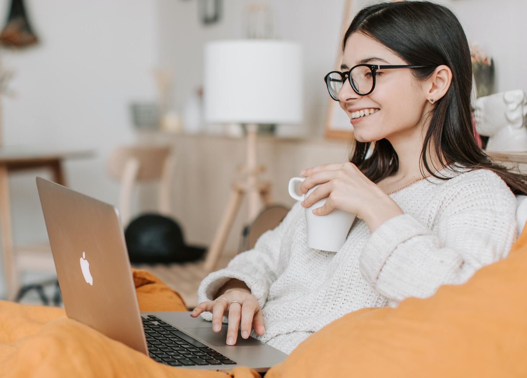 Adult in a calm, warm-lit home space holding a laptop mid-session, soft natural light
