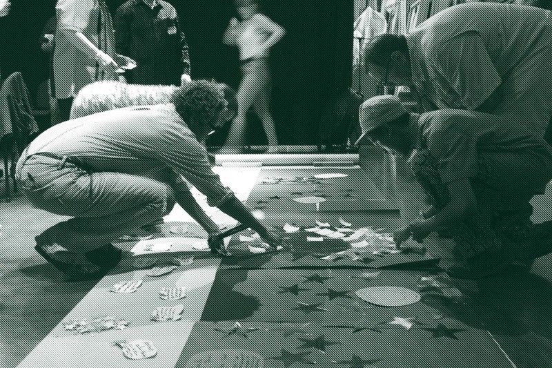 Four people kneel over posters with large cut out stars on the ground and engage in an acitivty together.