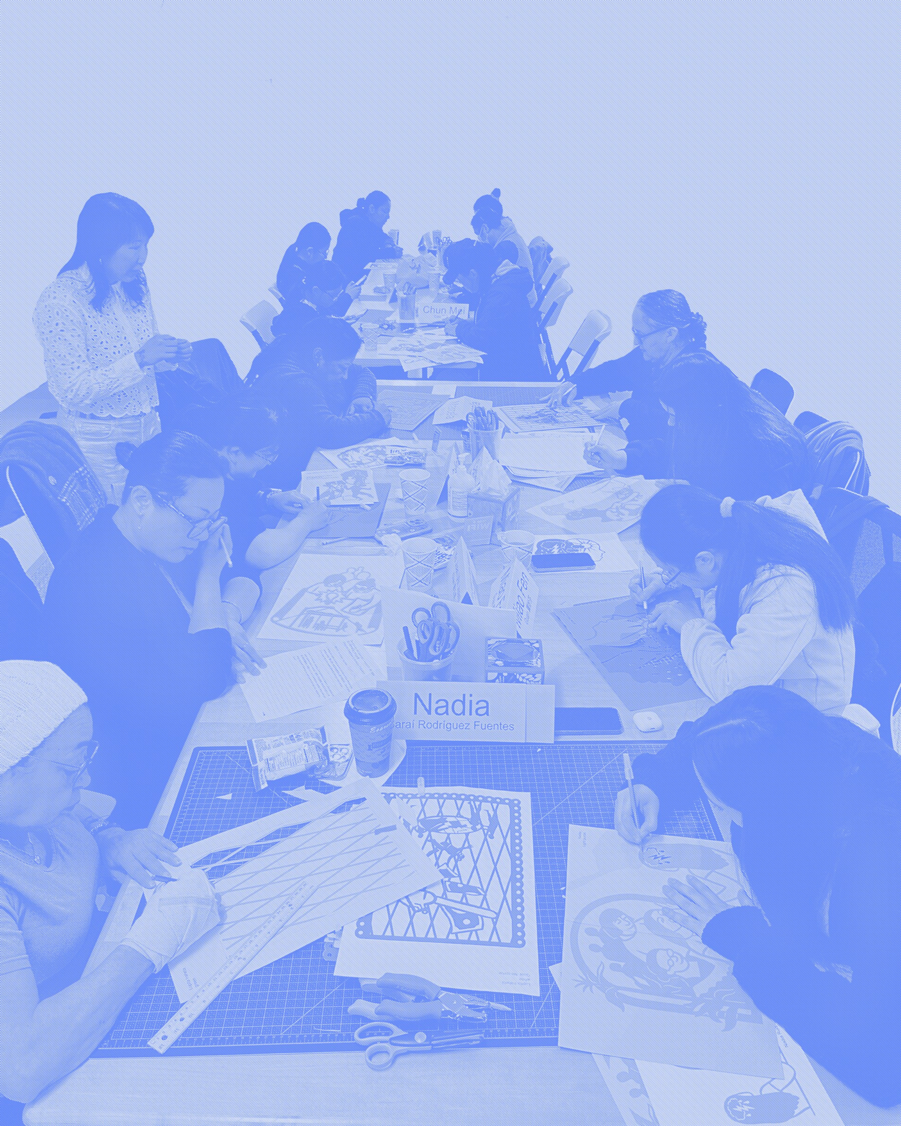 A group photo of many women at a table working on cut paper artworks. Artist Christine Wong Yap stands behind them. The photo is rendered in a periwinkle blue and white bitmap. 