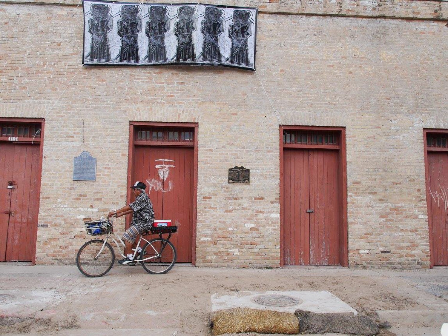 Buffalo Soldiers, 2016. Seen here is a block print of four Buffalo Soldiers in standing with their fists raised. Each wears a pin stating “Black Lives Matter”. Inspired by the 1906 Brownsville Affair in which 167 Buffalo Soldiers were dishonorably discharged after being falsely accused of murder. The print is installed on the side of a historic building in downtown Brownsville, just blocks away from where the Brownsville Affair took place. Project concept developed as part of Activating Vacancy Arts Incubator in collaboration with buildingcommunityWORKSHOP. Image: Christina Patiño Houle.