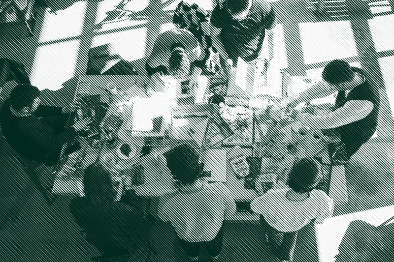 A birdseye view of a table covered with magazines and collage materials and surrounded by seven people making zines together.