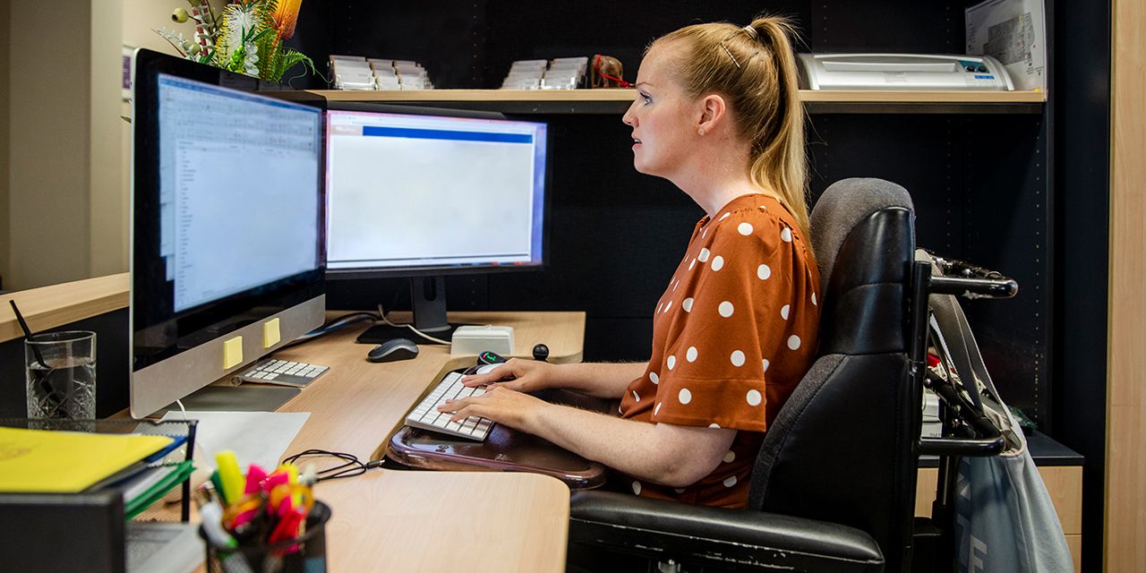 A person in an electric wheelchair using a computer. Photo.