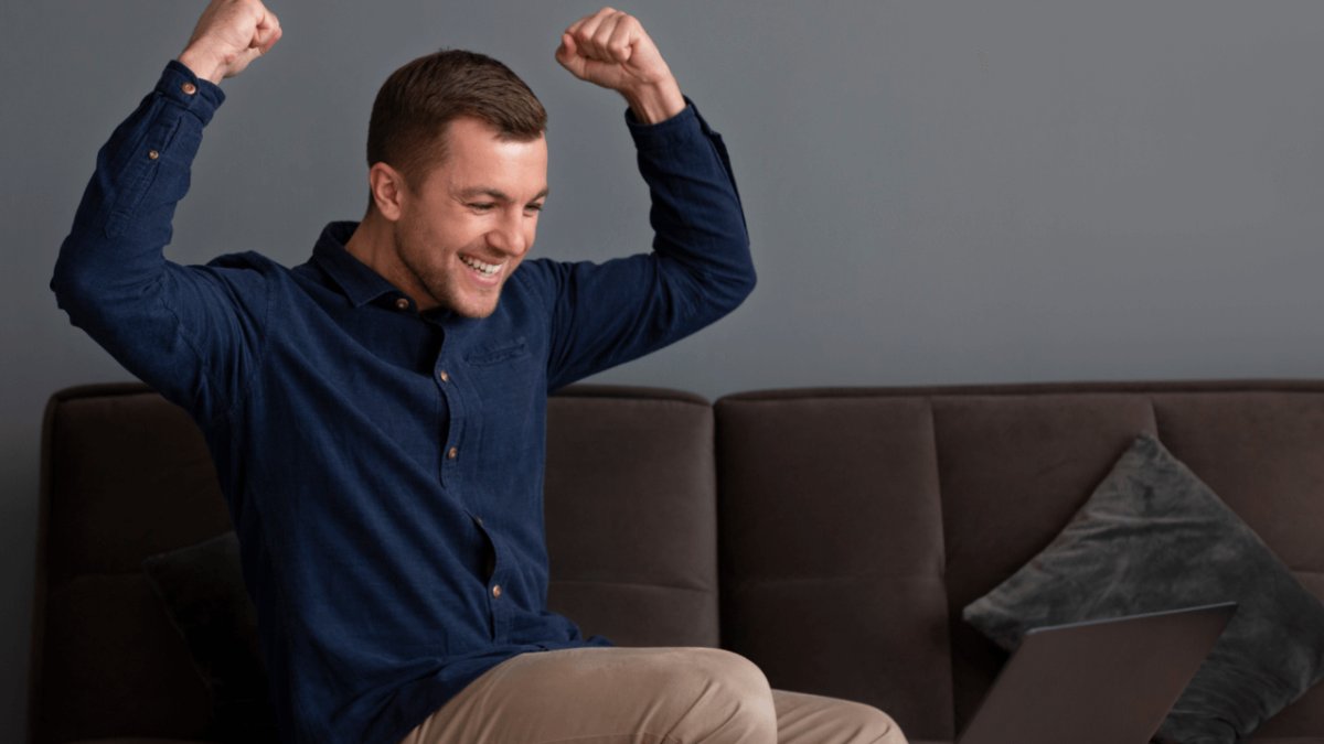 Man raising arms in celebration while looking at a laptop.