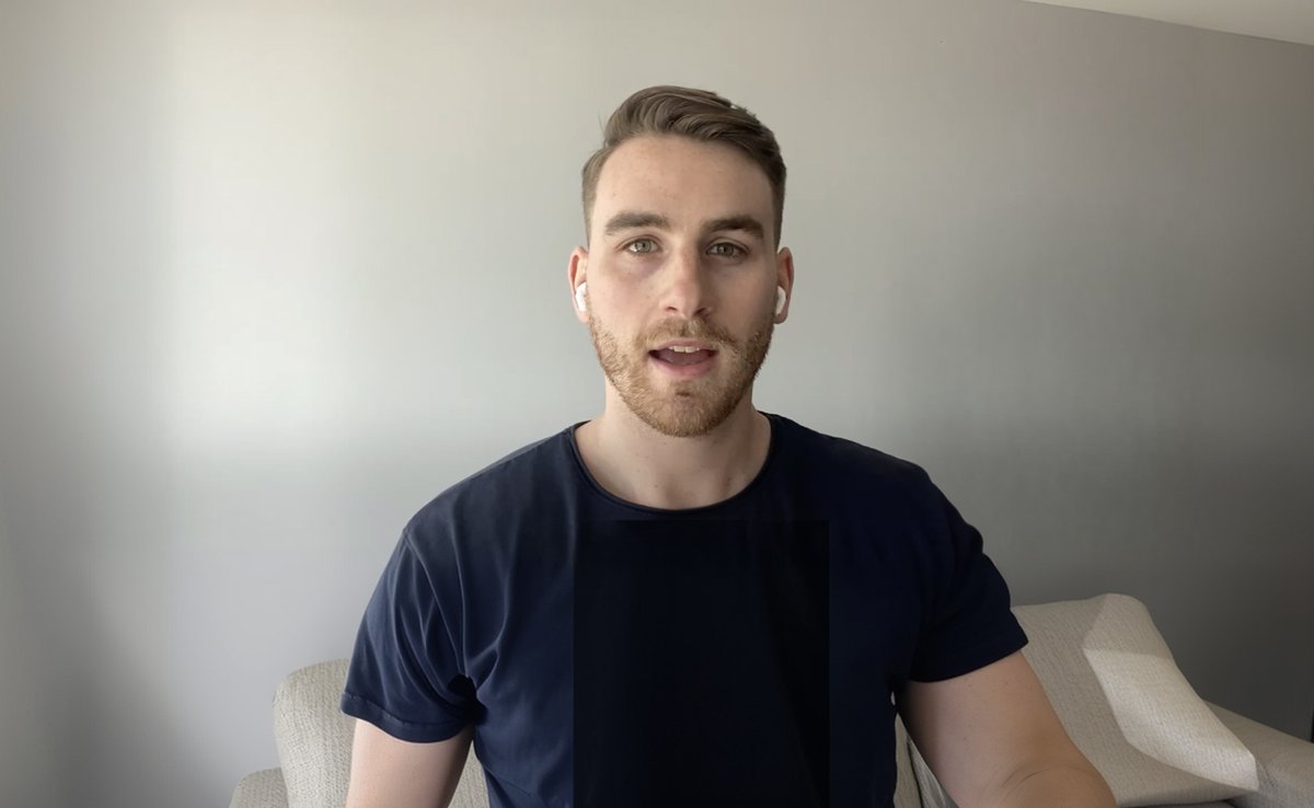 Young man with a beard, dark blue shirt, and white earbuds speaking to the camera.