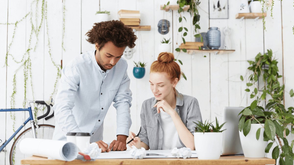 A man and a woman collaborate at a desk in a bright, plant-filled office.