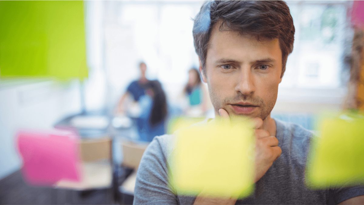A man with his hand on his chin looks intently at sticky notes on a clear board.