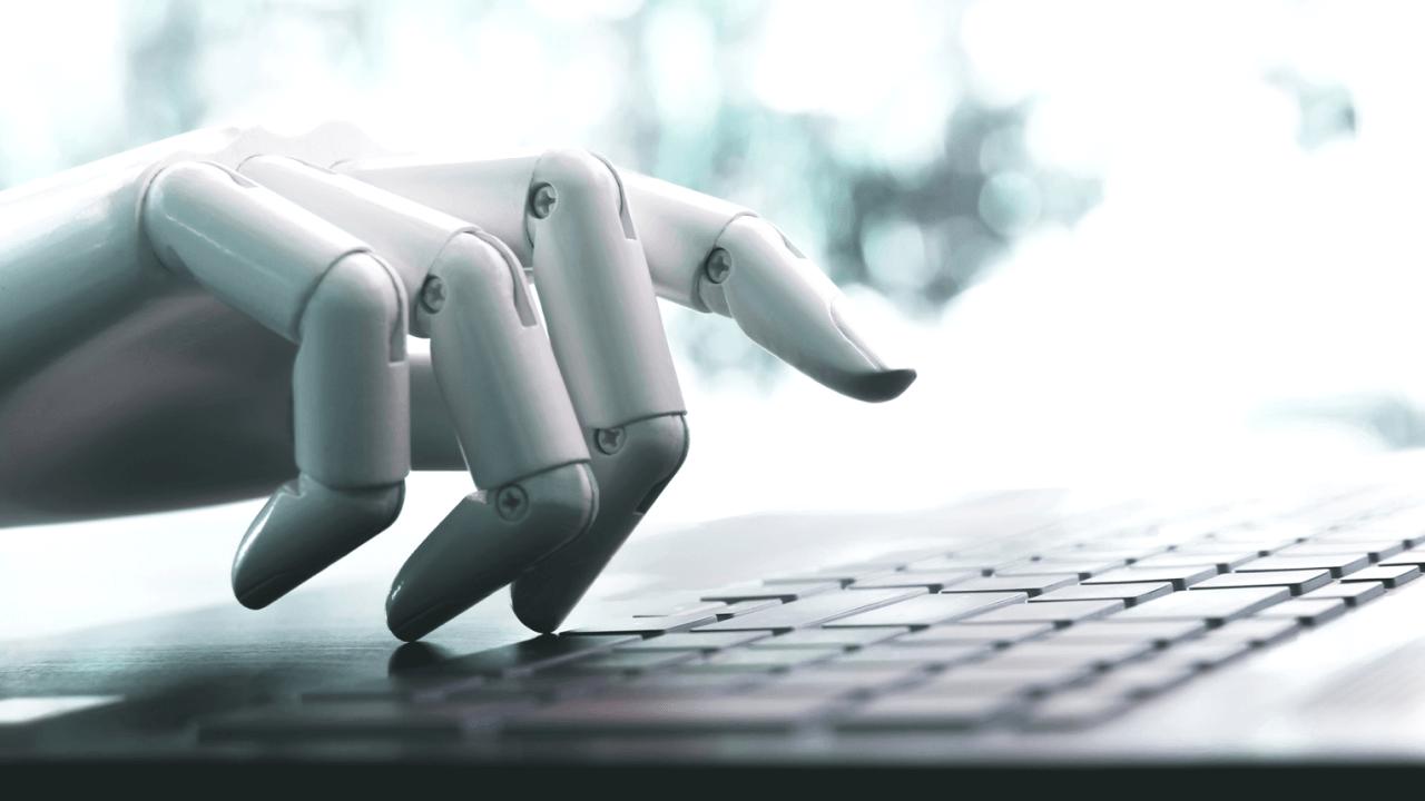 A white robotic hand poised over a laptop keyboard.