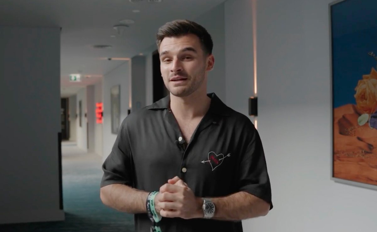 A man in a black shirt with a heart-and-arrow design stands in a hallway.