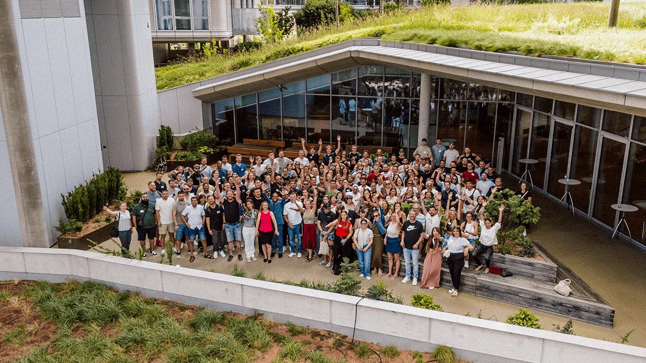 A large group of people posing outdoors in front of a modern building with a green roof.