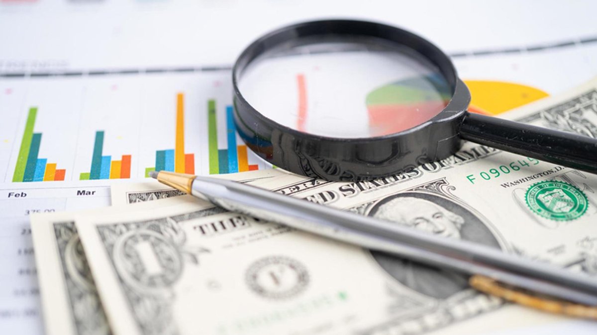 Magnifying glass, pen, and dollar bills on a document with colorful charts.