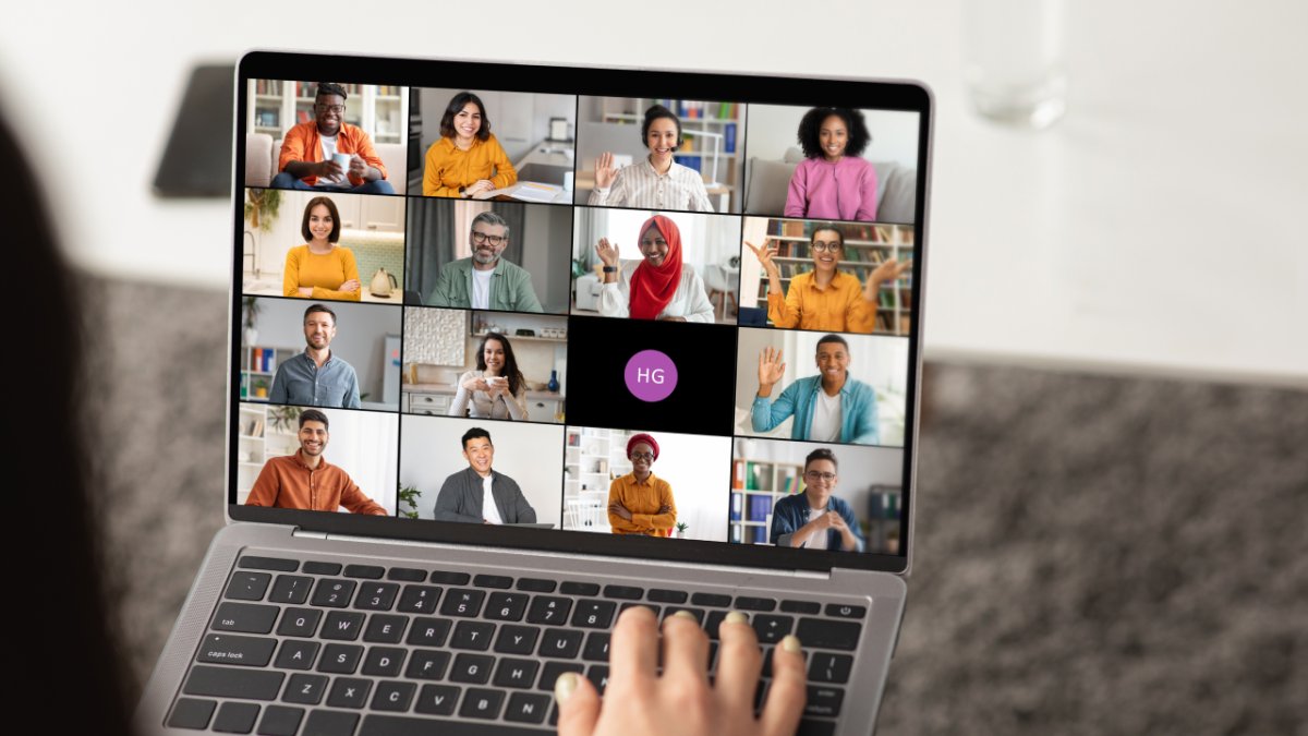 A person types on a laptop, displaying a video conference call with diverse participants on the screen.