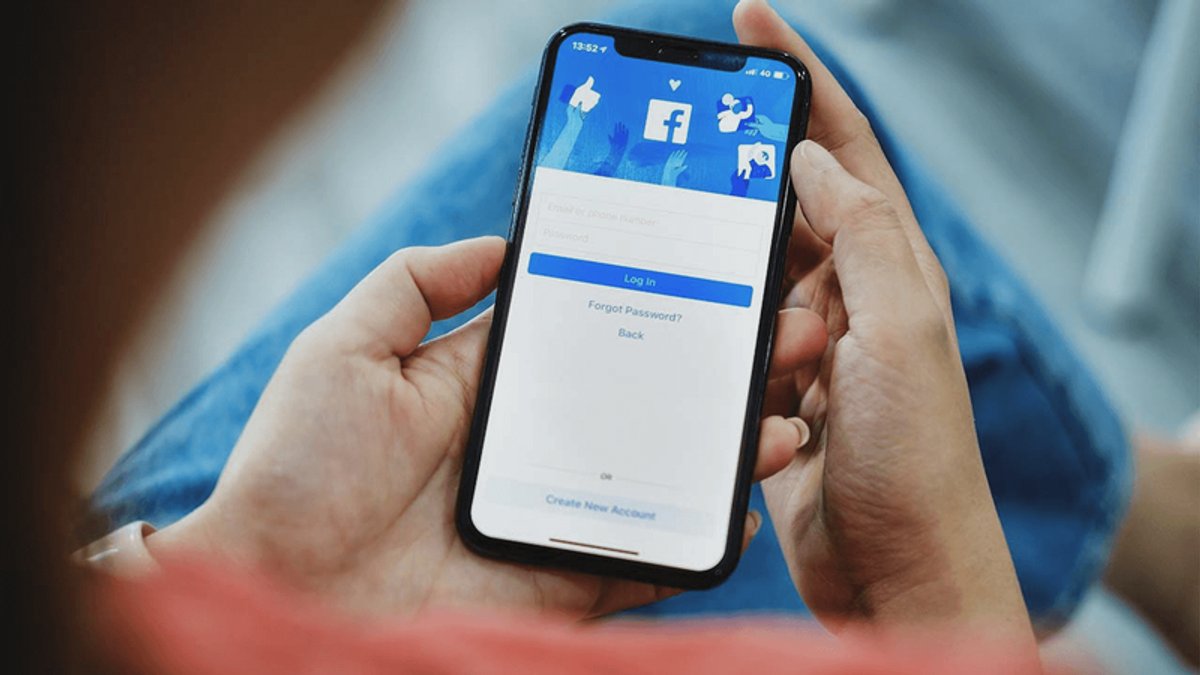 Hands hold a smartphone displaying the Facebook login screen.