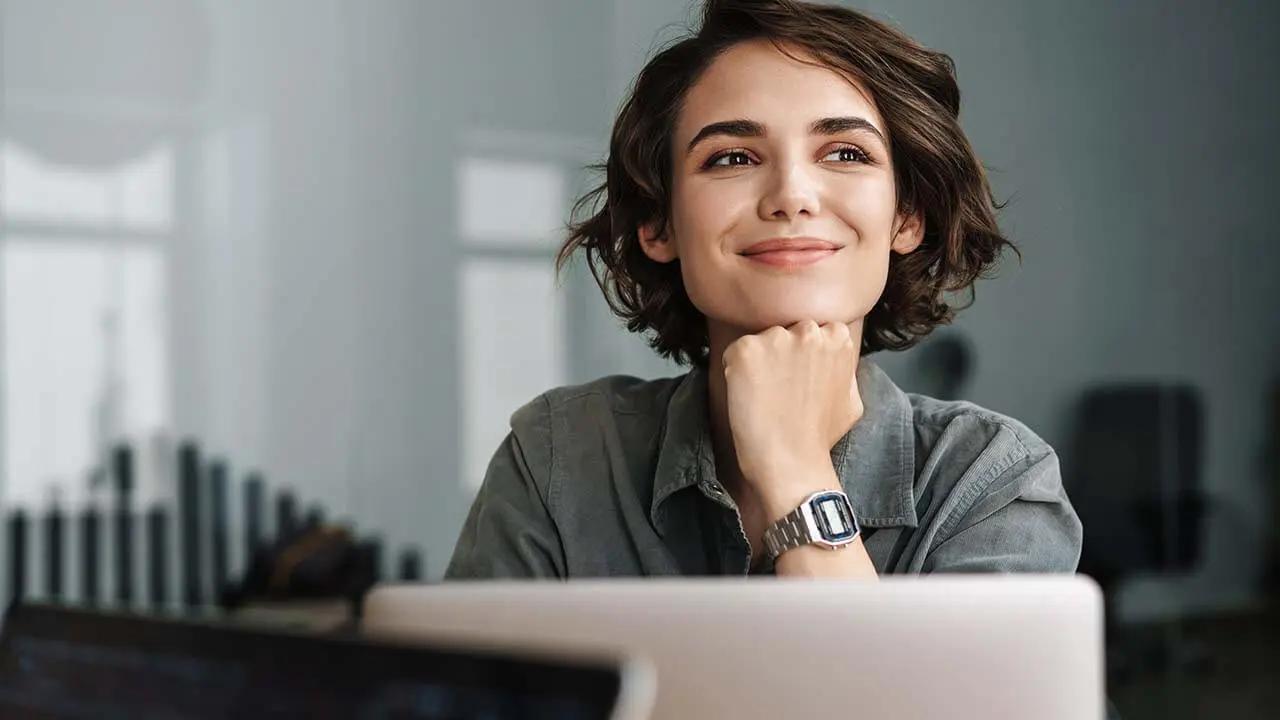 Smiling woman with short hair, chin resting on hand, looking thoughtfully up.
