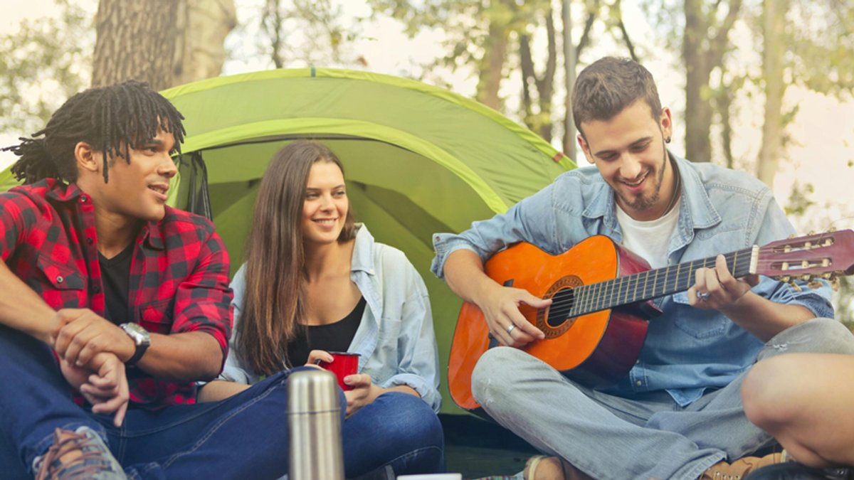 Three friends camping, one playing an acoustic guitar.