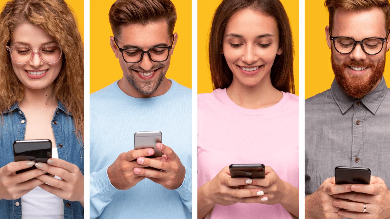 Four smiling young adults looking at their smartphones.