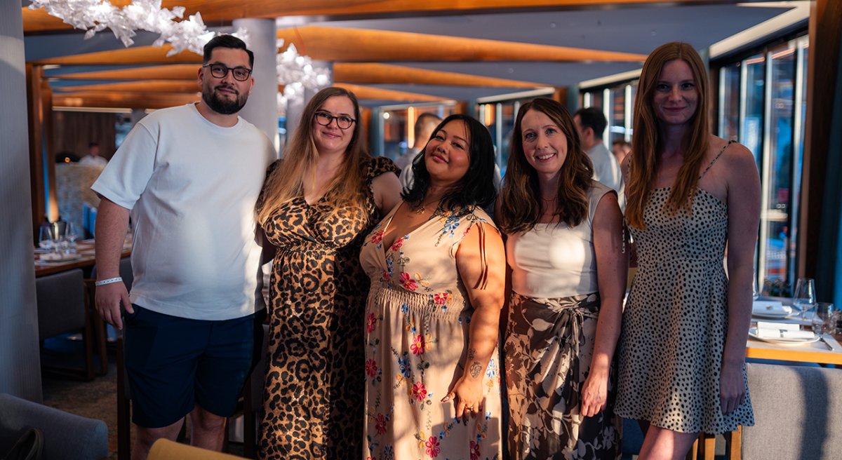 Smiling group of five people, including one man and four women, in a modern restaurant.