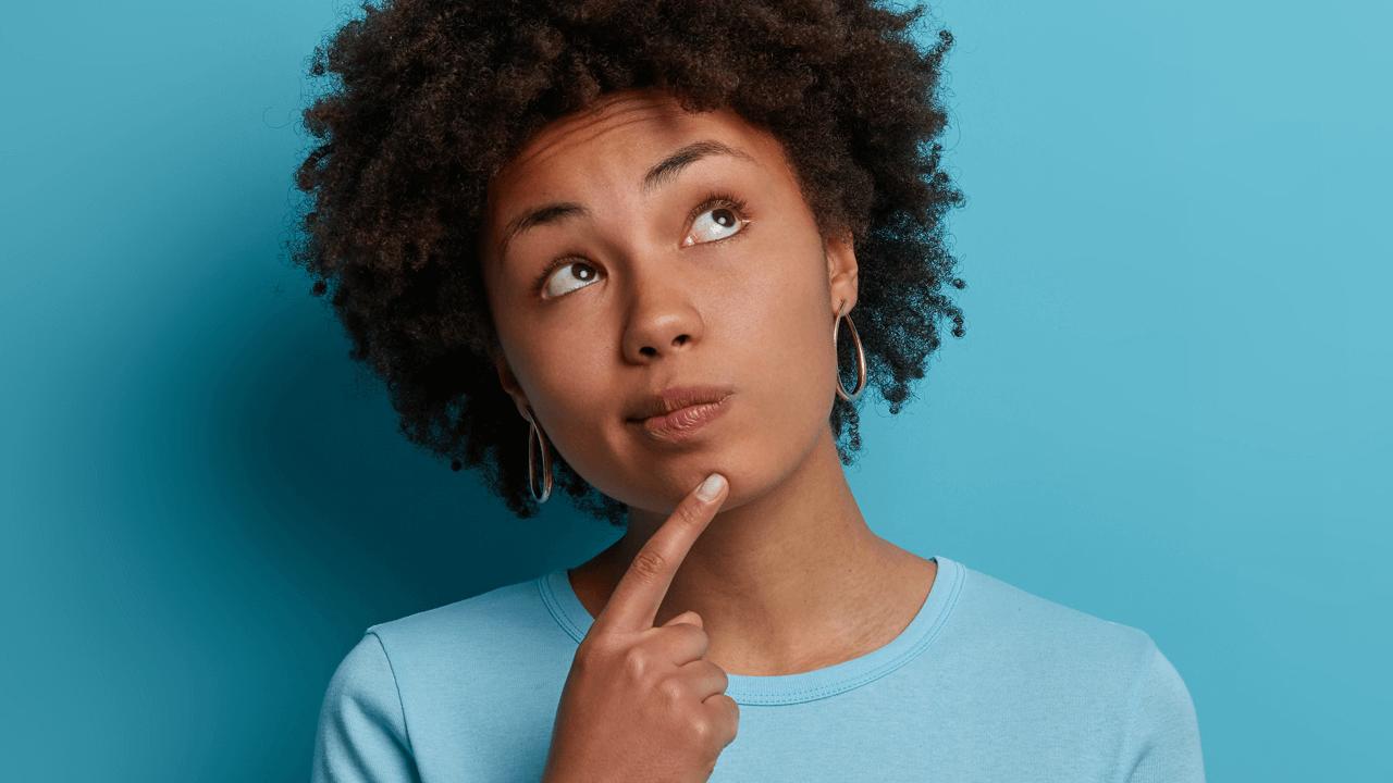 A young Black woman with curly hair looks up thoughtfully, finger on her chin, against a blue background.