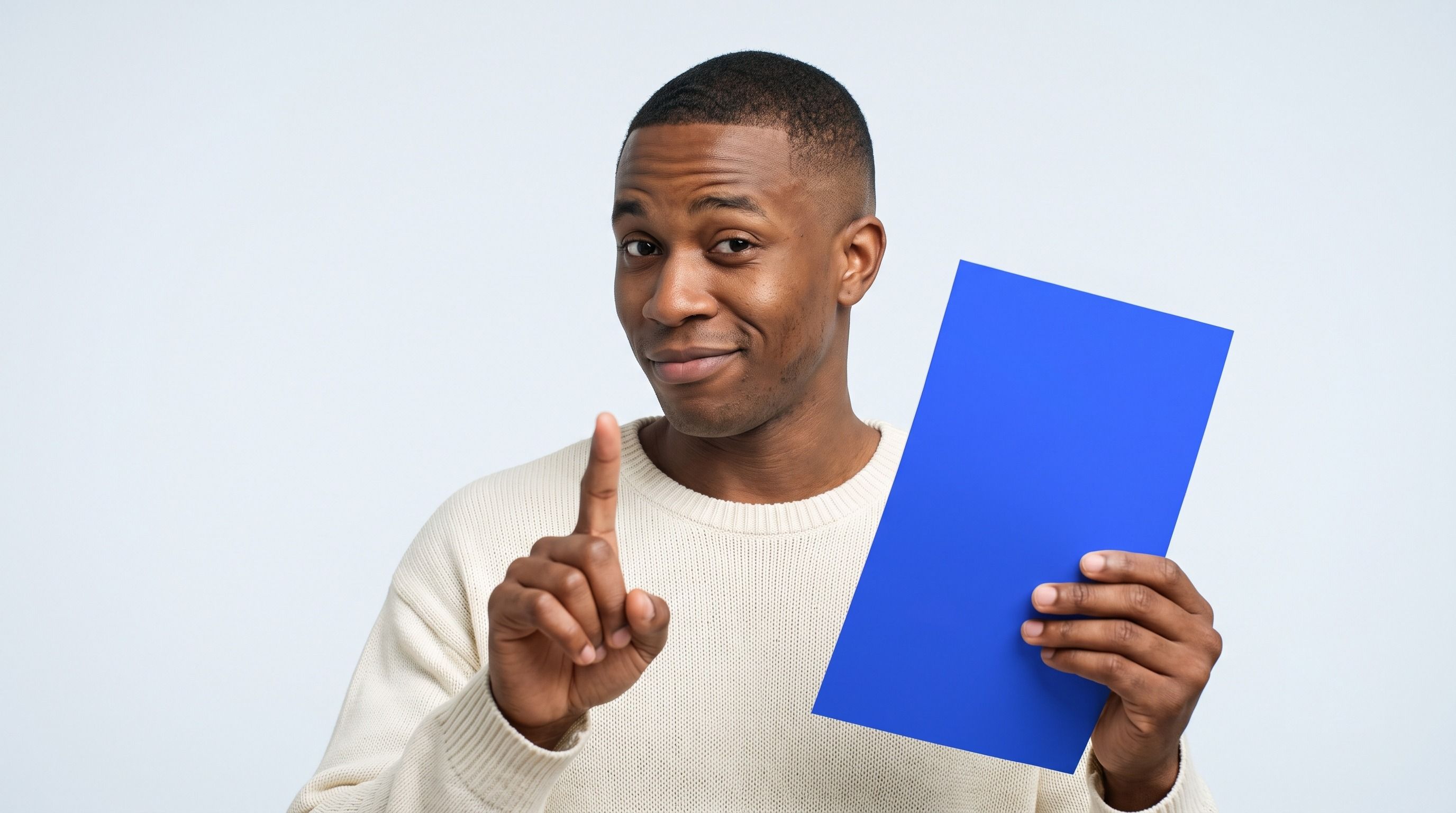 A Black man holds a blue card and raises his index finger, looking at the camera.