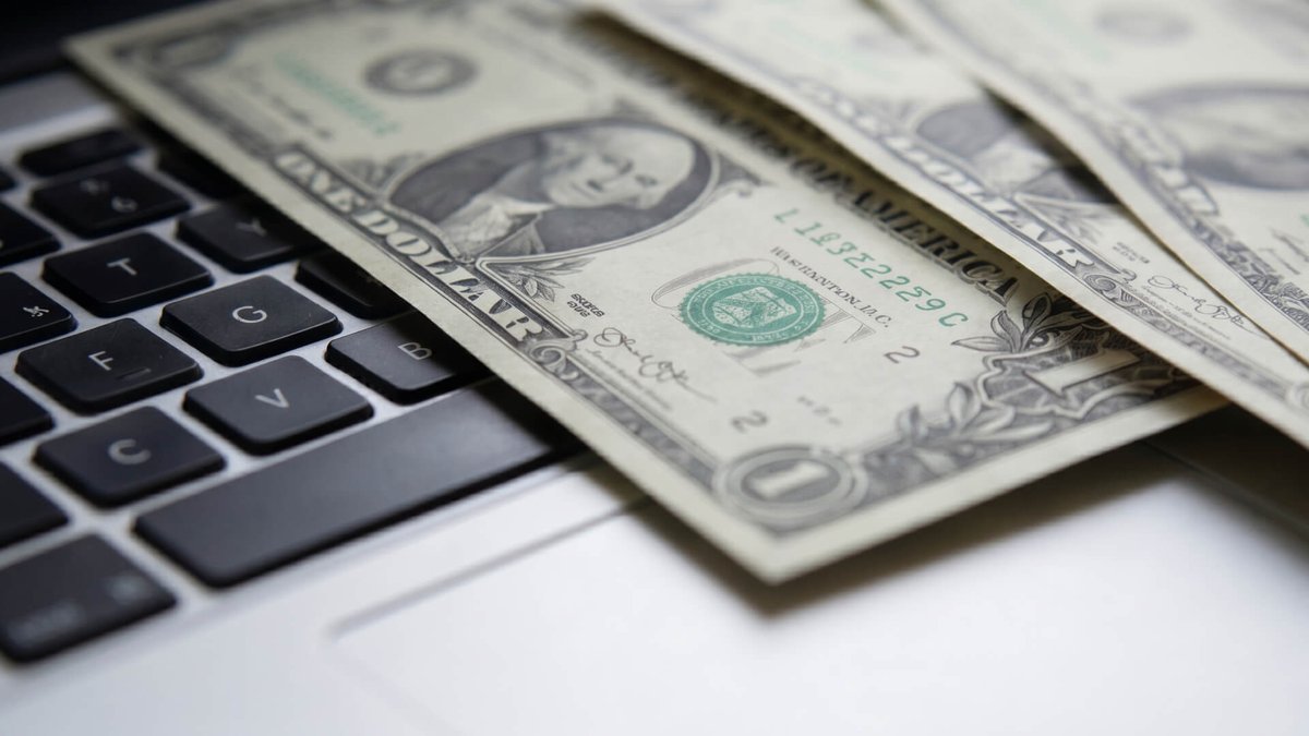 Several US one-dollar bills lying on a laptop keyboard.
