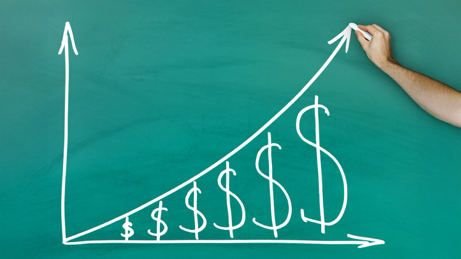 Hand drawing an upward financial growth graph with increasing dollar signs on a chalkboard.