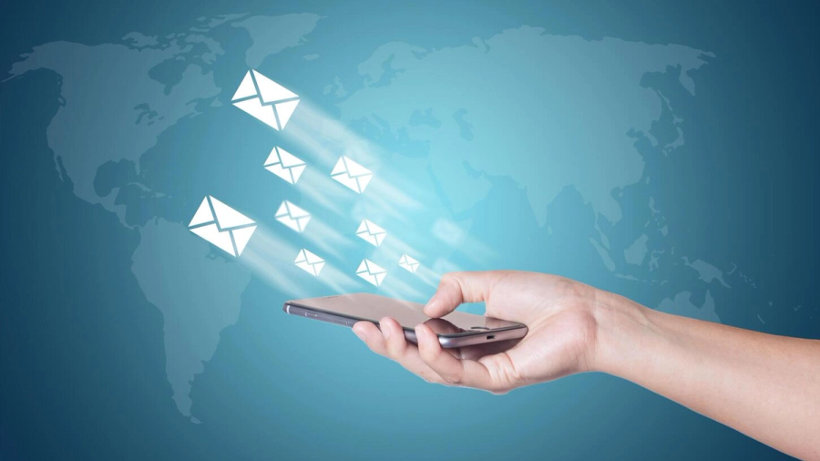 Hand holding a smartphone with email icons radiating over a global map.