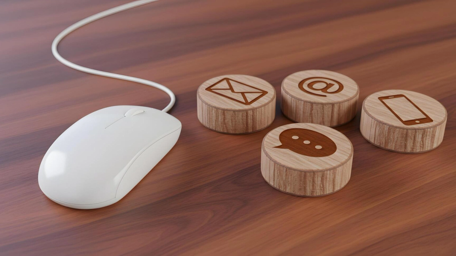 White computer mouse next to wooden blocks with contact icons for email, at-sign, chat, and phone.