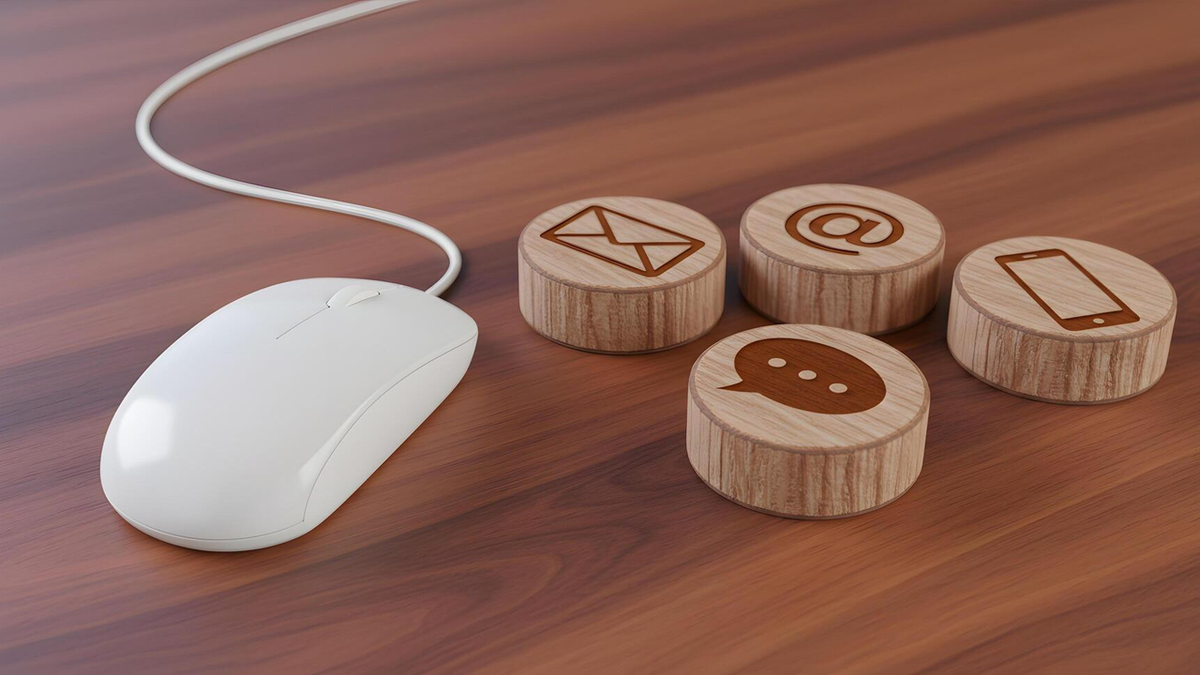 White computer mouse next to wooden blocks with contact icons for email, at-sign, chat, and phone.