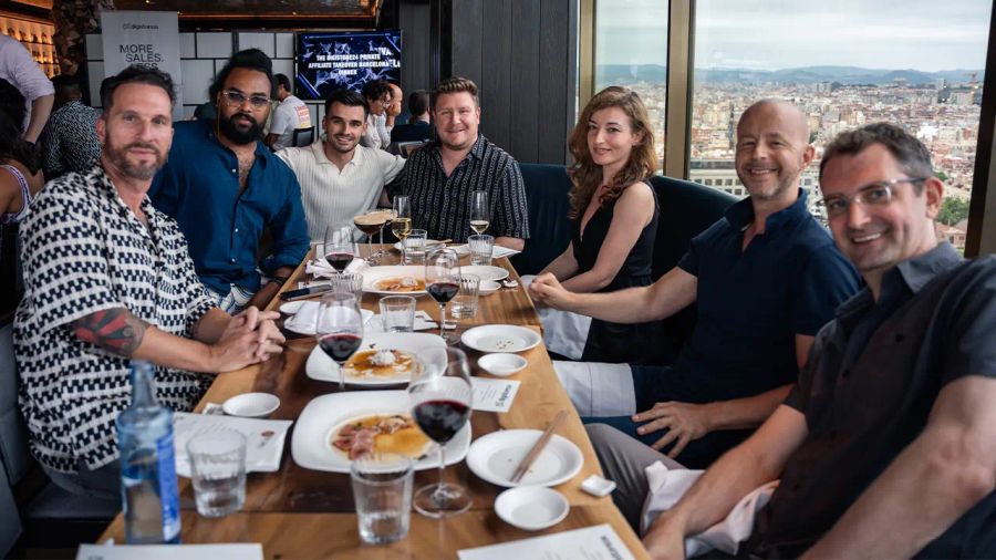 Eight people smiling at a dining table in a restaurant with a city view.
