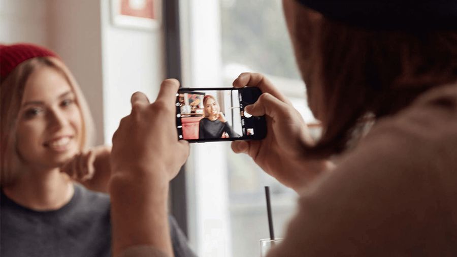 A person photographs a smiling woman with a smartphone, showing her image on the screen.