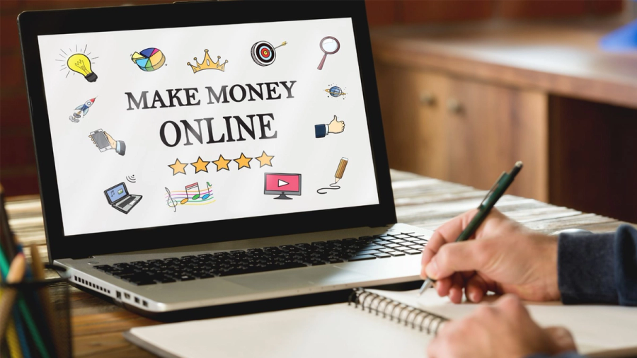 Laptop screen displays "MAKE MONEY ONLINE" with surrounding icons, next to a person writing in a notebook.