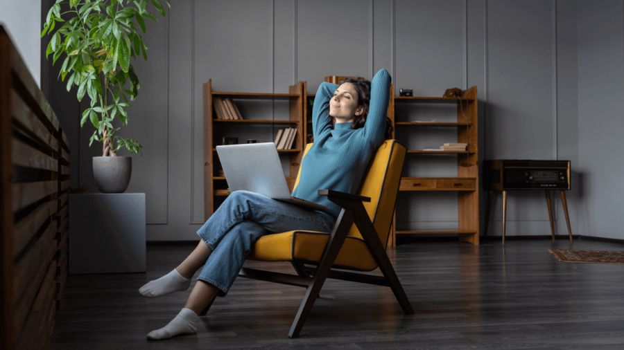 A woman relaxing in a yellow armchair with a laptop on her lap.
